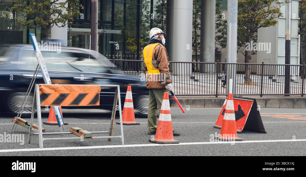 Traffic guard watches the flow of cars for a construction zone in central Tokyo Stock Photo