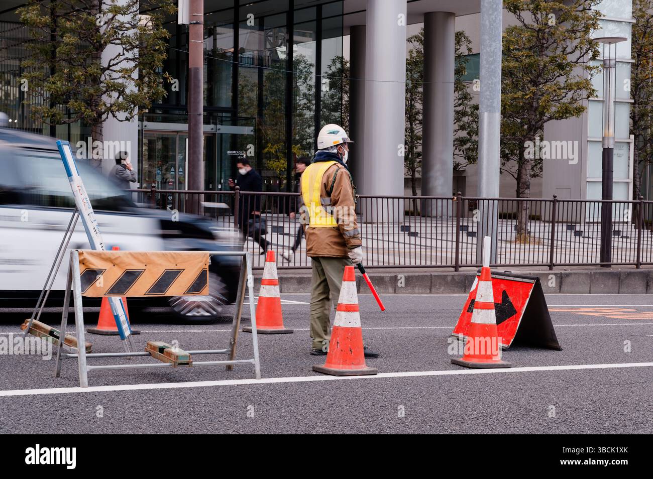Traffic guard stands alert amid cones and passing vehicles during urban roadwork Stock Photo