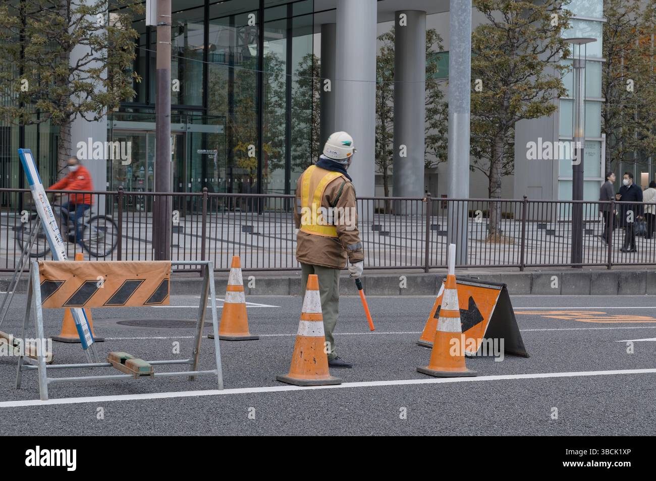 Construction worker stands alert amid traffic cones while guiding the morning flow with a red baton Stock Photo