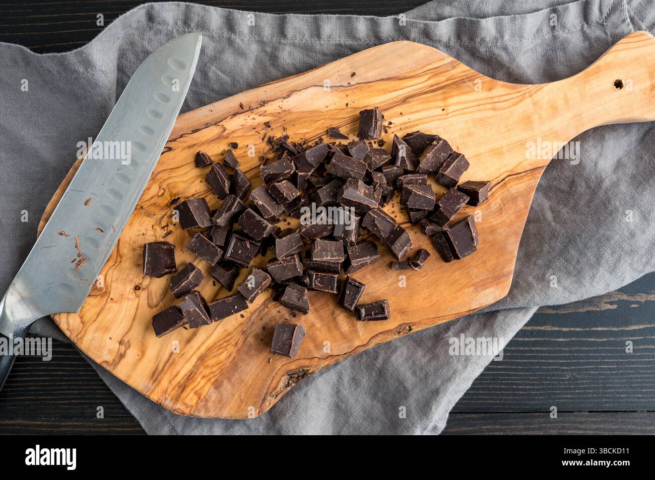 Chopped Bar of Baking Chocolate on Cutting Board: Chopped pieces of unsweetened chocolate on a wooden cutting board with knife Stock Photo