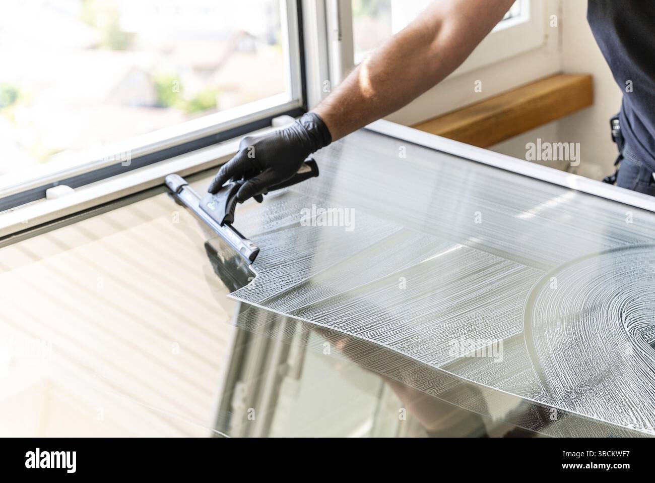 A professional cleaner using a squeegee and scraper to clean a large apartment window Stock Photo