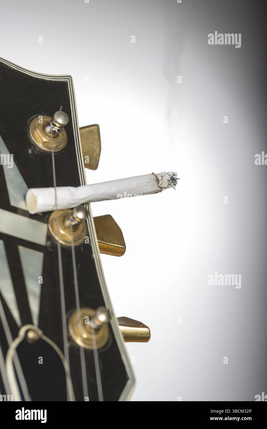 cigarette in guitar strings close up of a guitar headstock with burning cigarette sticking under one  string Stock Photo