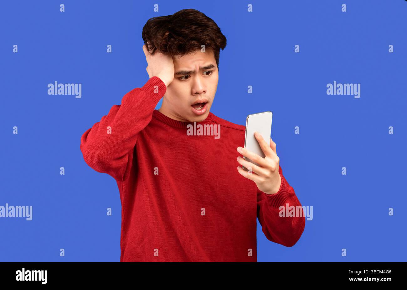 Surprised asian man using mobile phone on blue wall Stock Photo