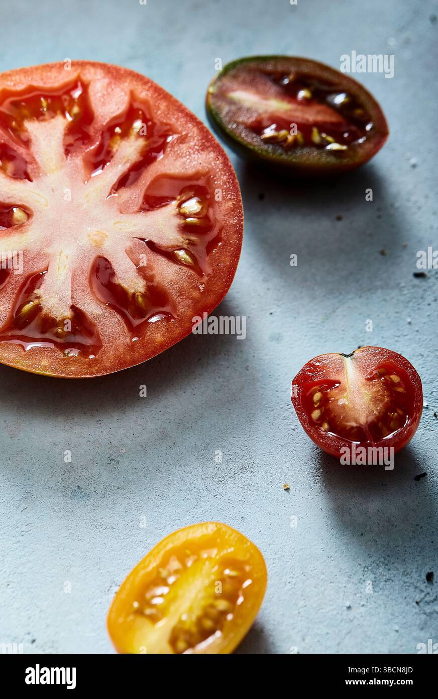 Assorted sliced tomatoes on a light blue textured surface Stock Photo