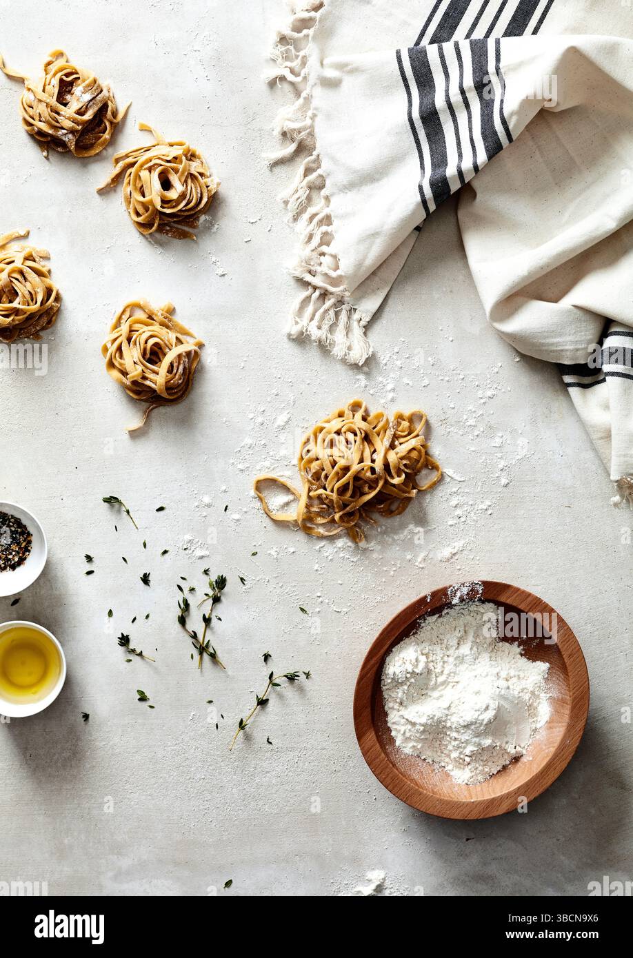 Hands shaping fresh pasta nests on floured surface with herbs Stock ...