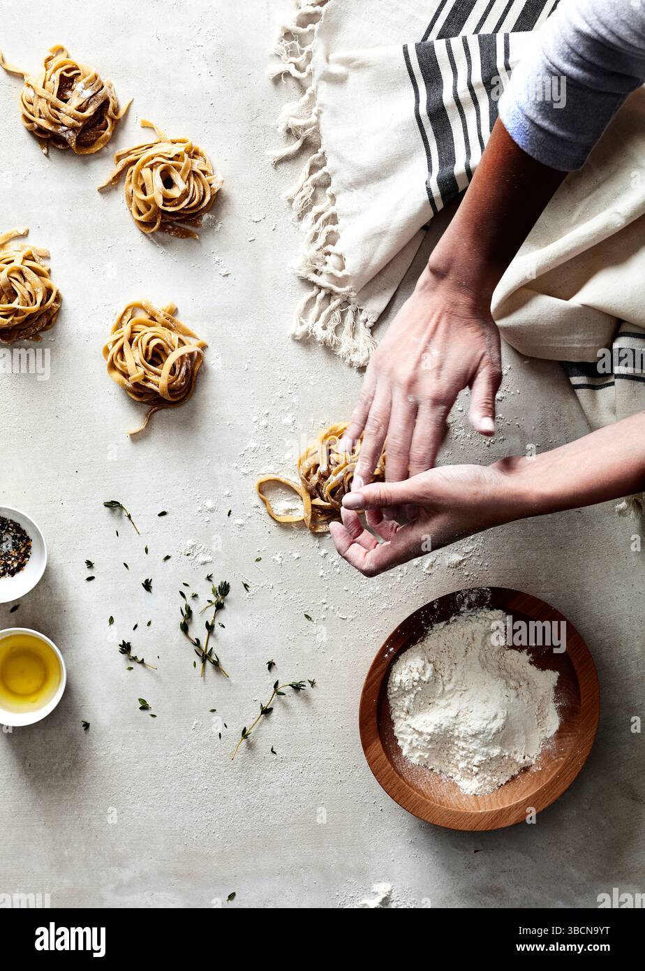 Hands shaping fresh pasta nests on floured surface with herbs Stock ...