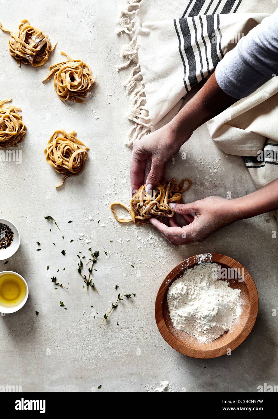 Hands shaping fresh pasta nests on floured surface with herbs Stock ...