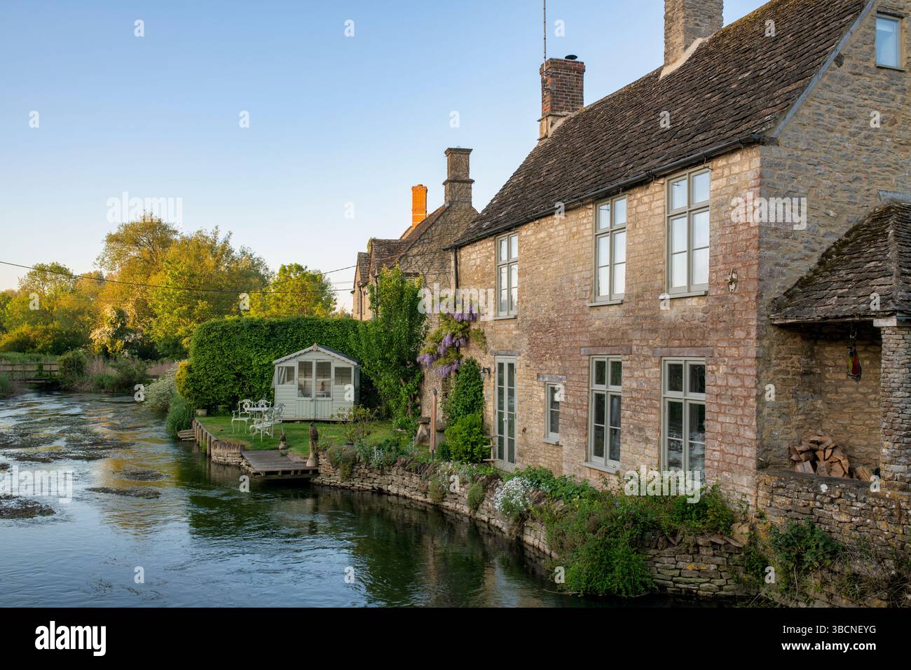 Stone cottage on the river coln in the early morning just after sunrise. Fairford, Cotswolds, Gloucestershire, England Stock Photo