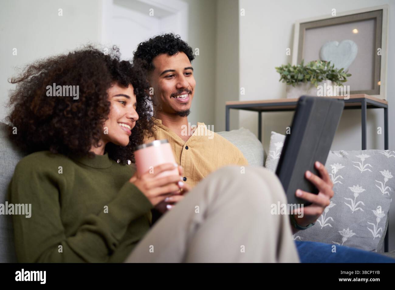 Young Couple Relaxing on a Couch at Home While Using a Tablet Stock Photo