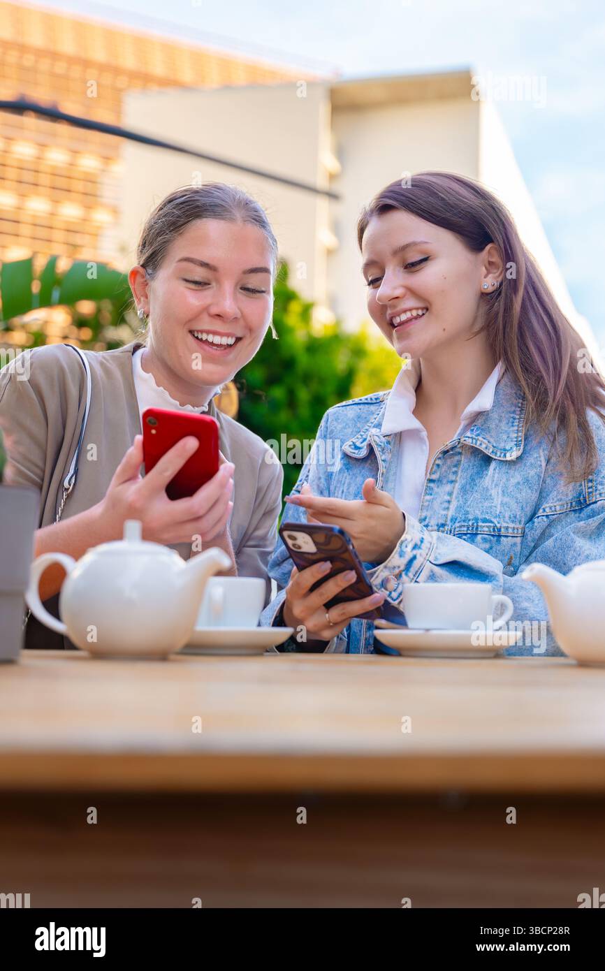 Two caucasian women using smartphones while enjoying tea at outdoor cafe table Stock Photo