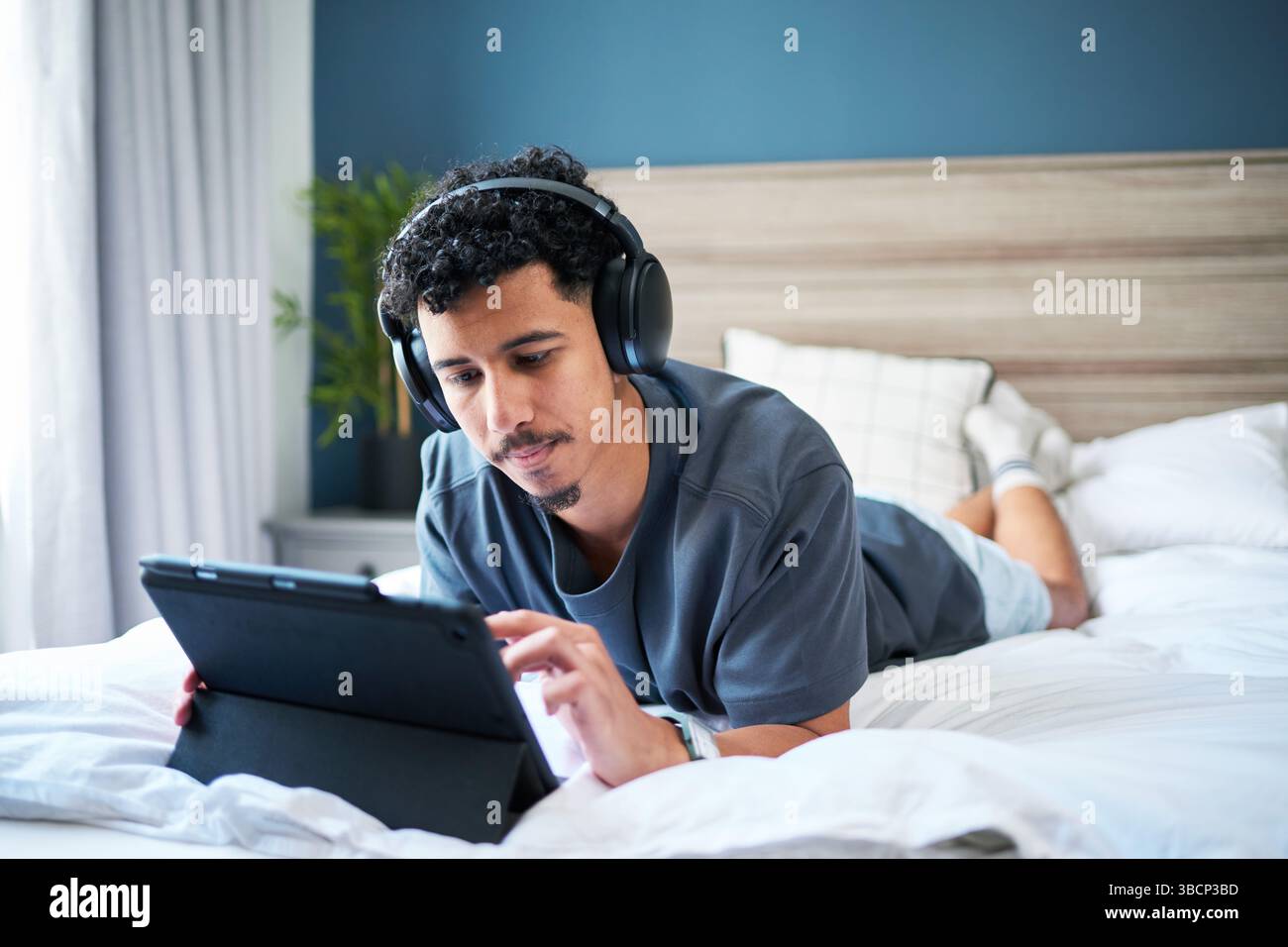 Relaxed Man Using a Tablet With Headphones in a Comfortable Bedroom Setting Stock Photo