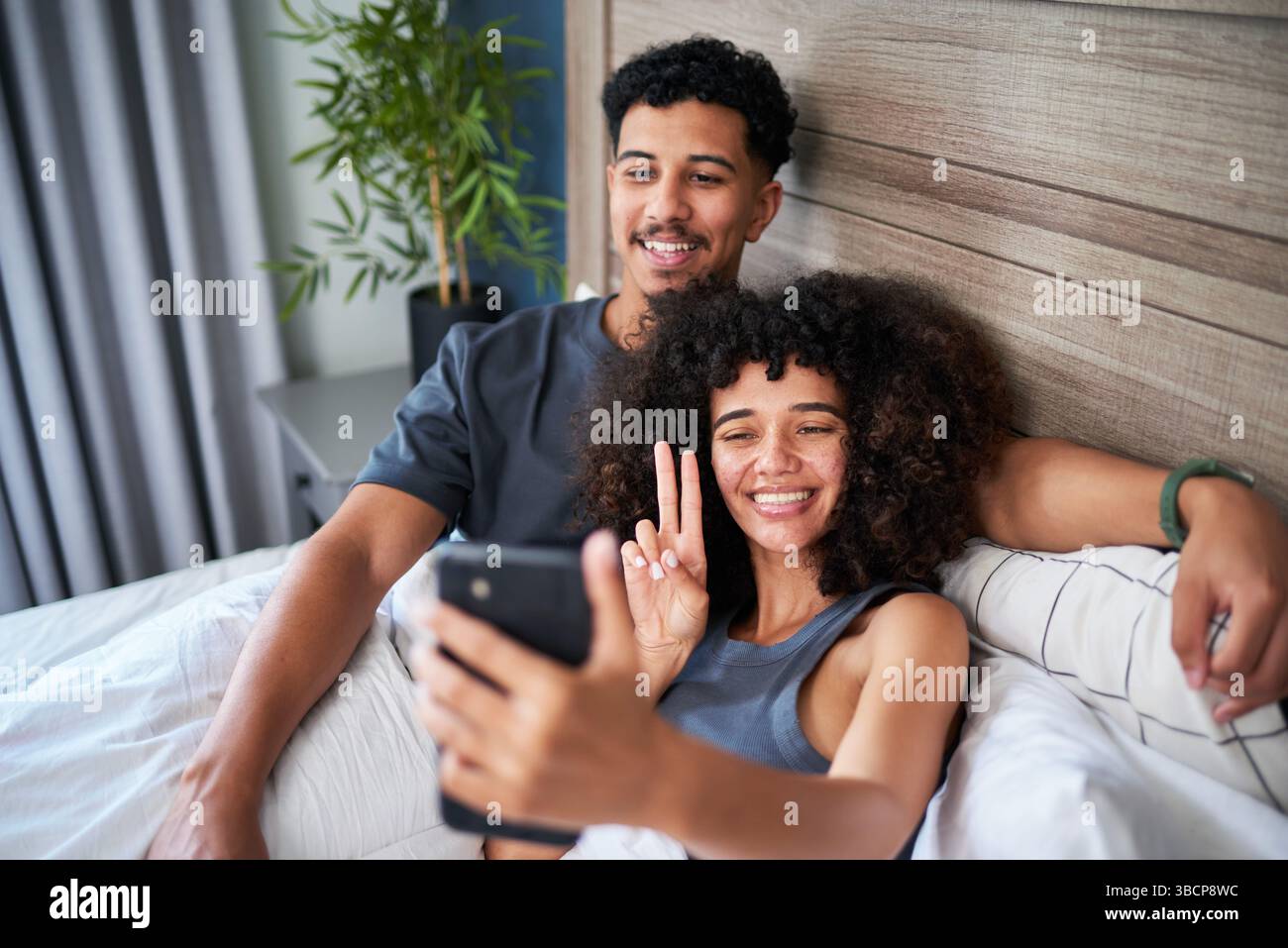 Couple Sitting Together on a Bed Relaxing and Taking a Selfie at Home Stock Photo