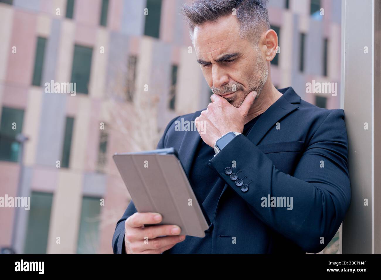 Thoughtful mature man using digital tablet while leaning on pole in city Stock Photo