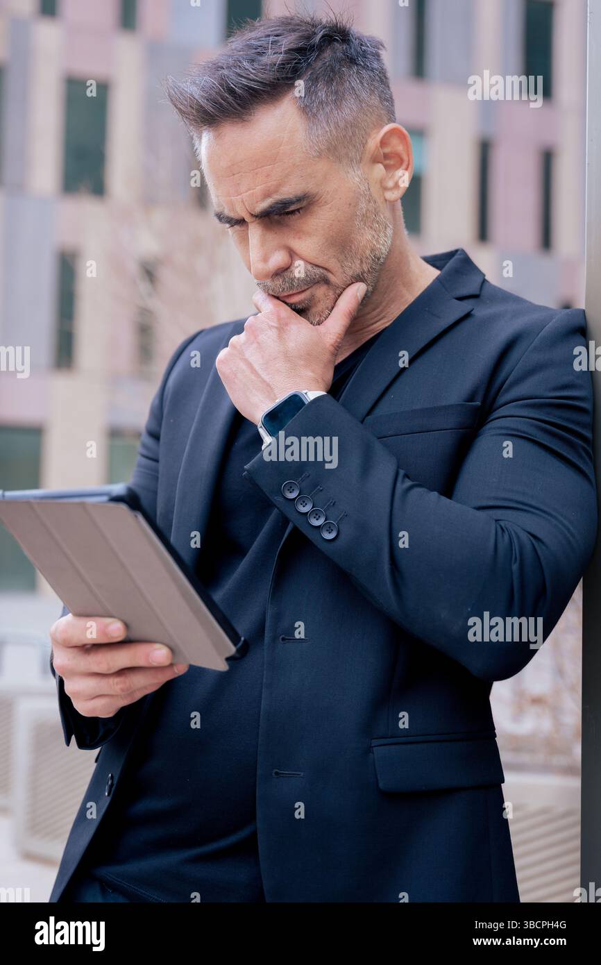 Thoughtful mature man using tablet while leaning on pole in city.Vertical Stock Photo