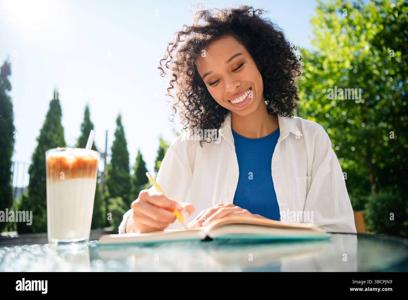 Charming young woman enjoying a sunny day with an iced coffee outdoors ...