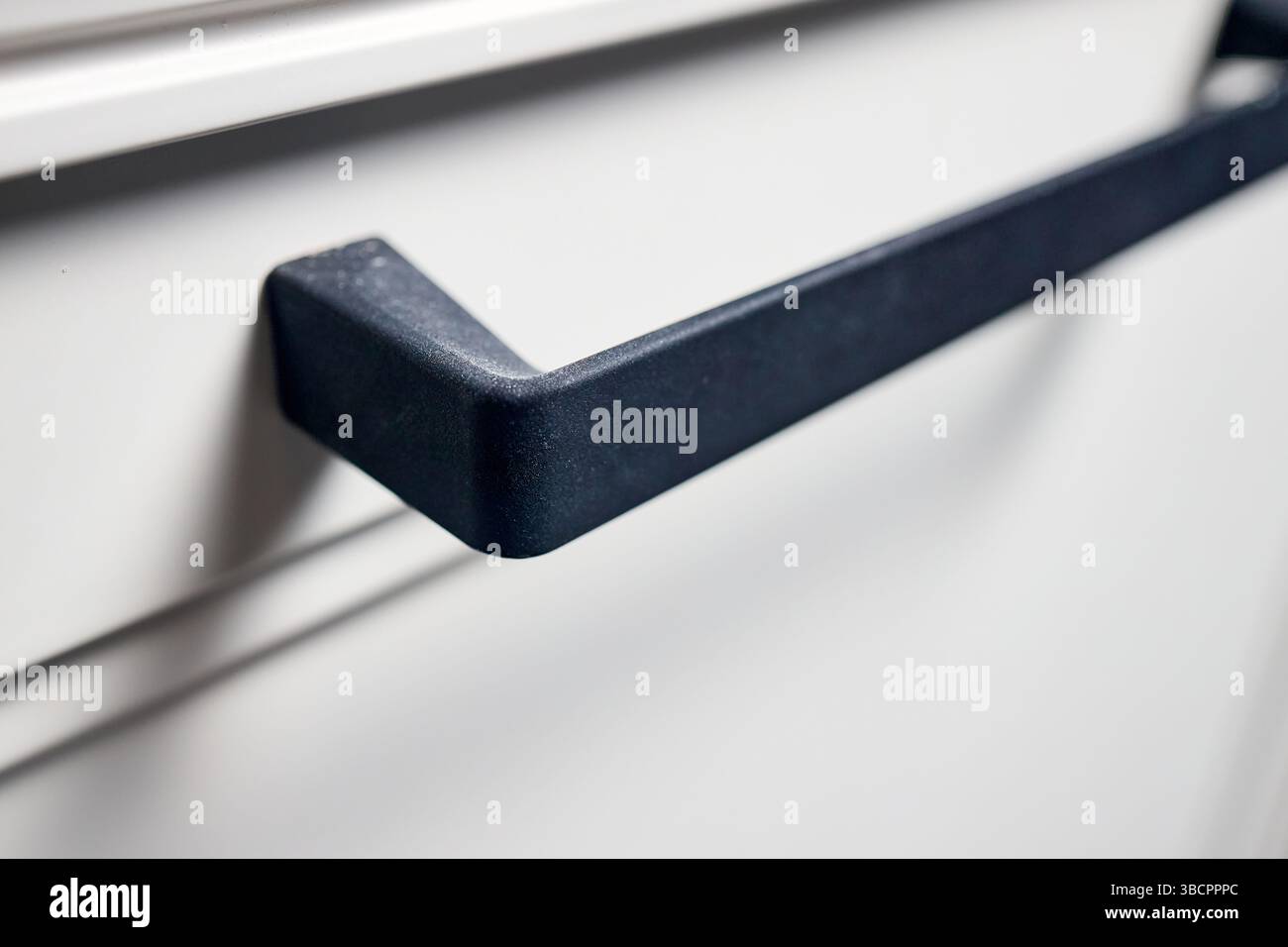 Kitchen cabinet drawer handle closeup. Black metal drawer handle selective focus horizontal shot. Kitchen contemporary interior element. Stock Photo