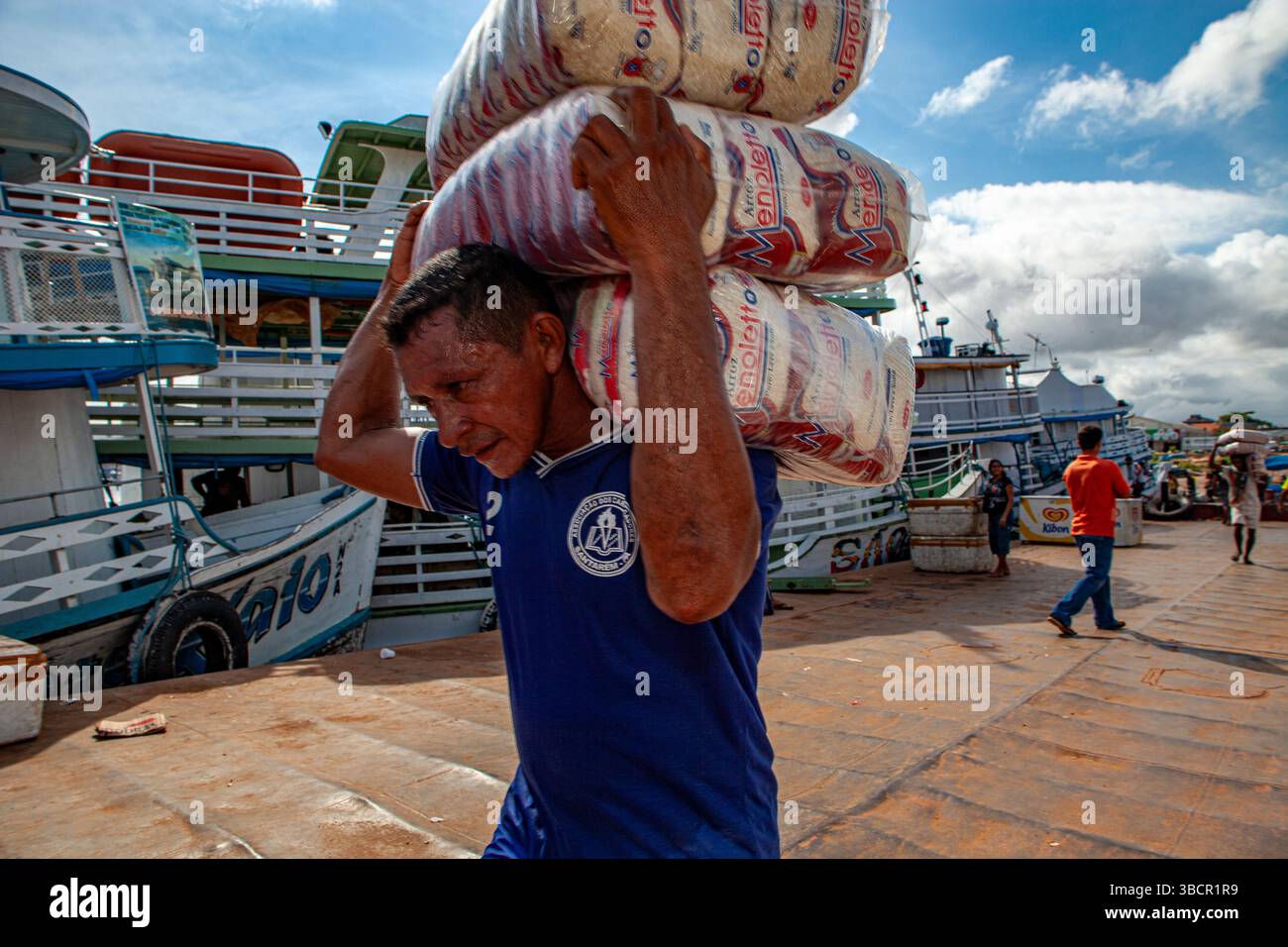 Dockworker loads packages of rice onto traditional Amazon riverboats at the Port of Santarém in Pará, Brazil. Stock Photo