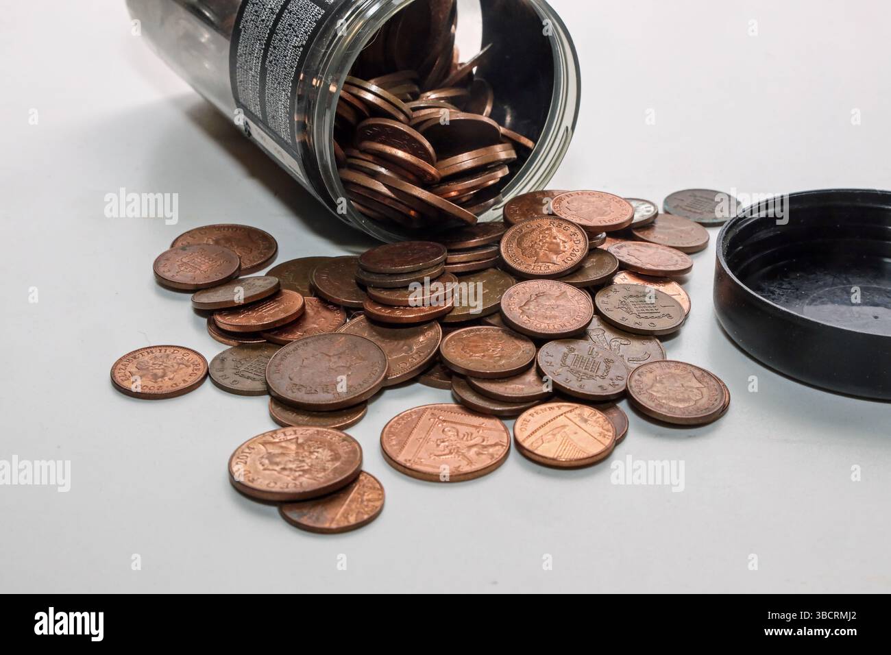 Small change, penny and twopenny coins, pouring out of a jar on a plain ...