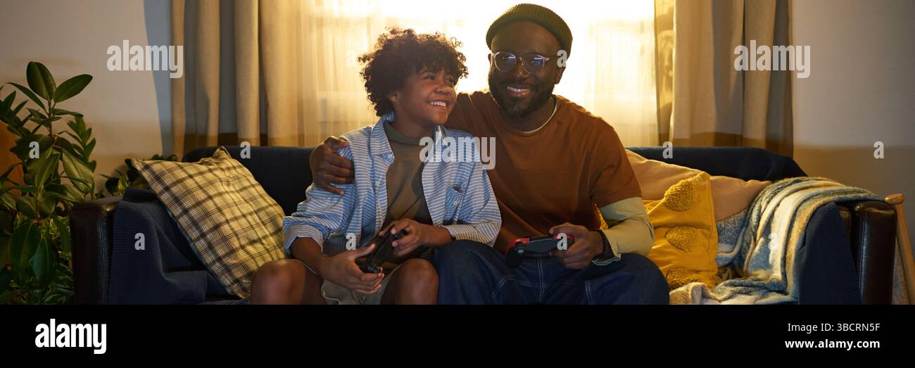 Father and Son Smiling While Playing Video Games Stock Photo