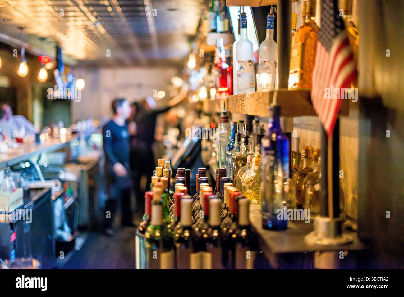 Virtue Feed And Grain Bar Alexandria Virginia // ALEXANDRIA, Virginia — The busy bar at Virtue Feed and Grain restaurant buzzes with activity in Old Town Alexandria. Located in a renovated 19th-century warehouse that once served as a feed and grain store, the bar area features industrial-inspired design elements that honor the building's utilitarian past. Patrons gather at the wooden bar counter where bartenders prepare craft cocktails and serve beverages in this popular Old Town establishment. Stock Photo