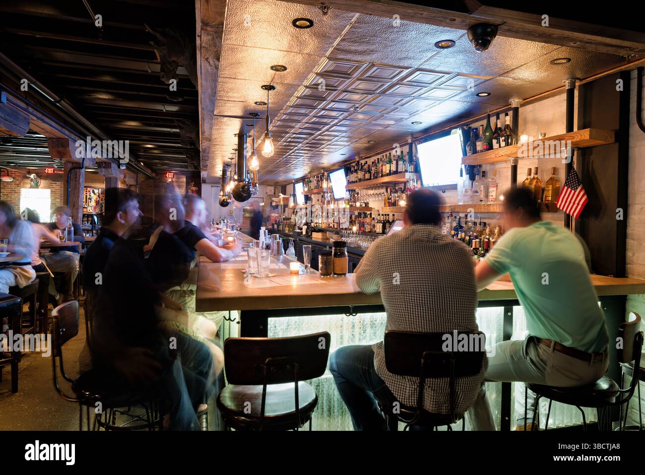 Virtue Feed And Grain Bar Old Town Alexandria Virginia // ALEXANDRIA, Virginia — The busy bar at Virtue Feed and Grain restaurant buzzes with activity in Old Town Alexandria. Located in a renovated 19th-century warehouse that once served as a feed and grain store, the bar area features industrial-inspired design elements that honor the building's utilitarian past. Patrons gather at the wooden bar counter where bartenders prepare craft cocktails and serve beverages in this popular Old Town establishment. Stock Photo