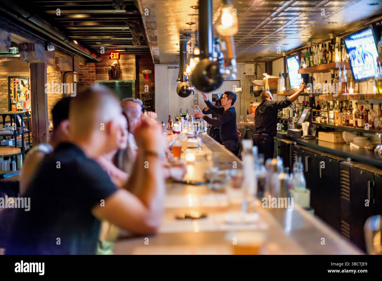 Virtue Feed And Grain Bar Old Town Alexandria Virginia // ALEXANDRIA, Virginia — The busy bar at Virtue Feed and Grain restaurant buzzes with activity in Old Town Alexandria. Located in a renovated 19th-century warehouse that once served as a feed and grain store, the bar area features industrial-inspired design elements that honor the building's utilitarian past. Patrons gather at the wooden bar counter where bartenders prepare craft cocktails and serve beverages in this popular Old Town establishment. Stock Photo