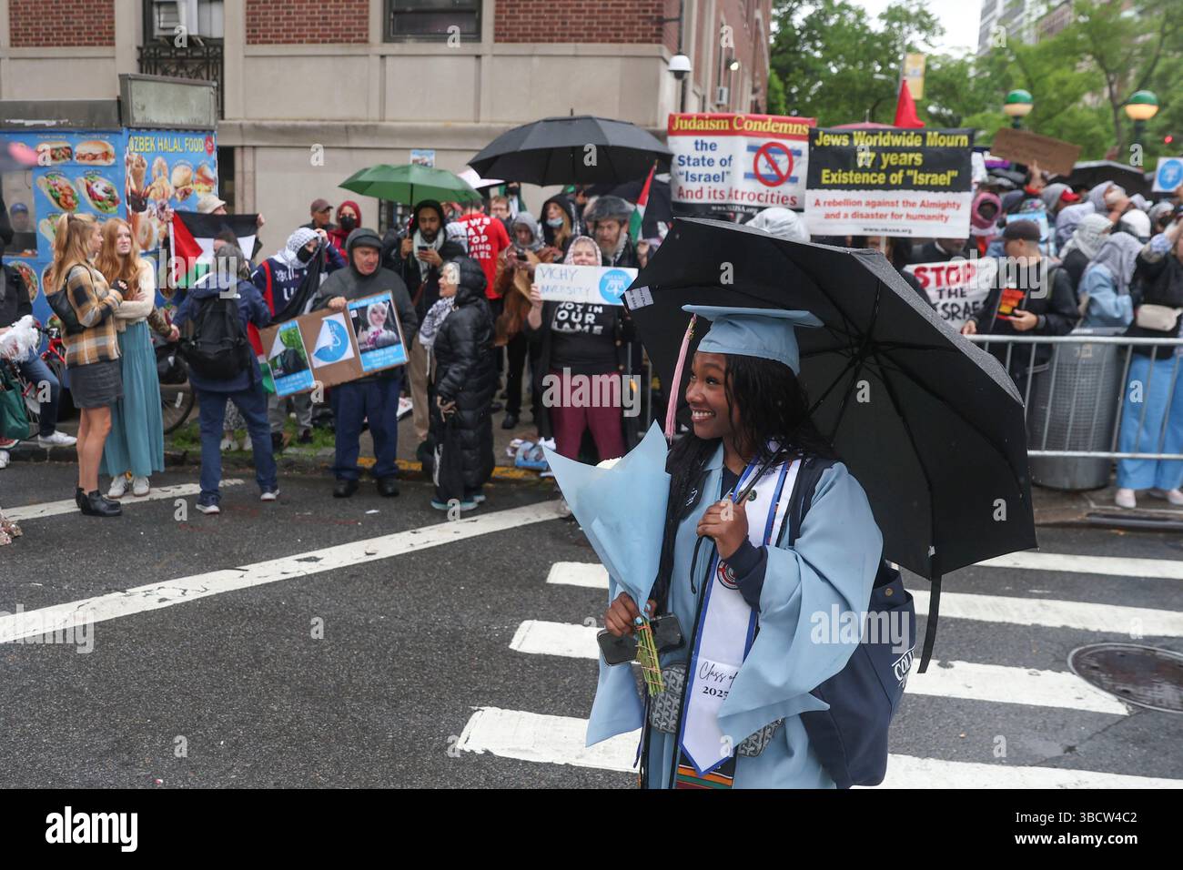 A graduate poses for a photo in front of a group of people protesting ...