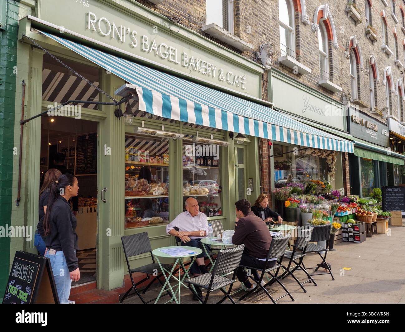 People eating outdoors at Roni's cafe pavement tables in Primrose Hill, Camden, London, UK Stock Photo