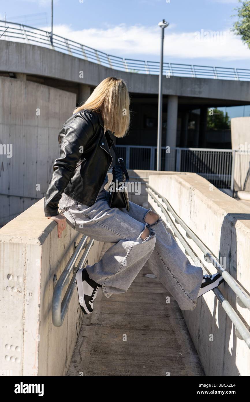Fashionable woman wearing a leather jacket and ripped jeans relaxes on ...