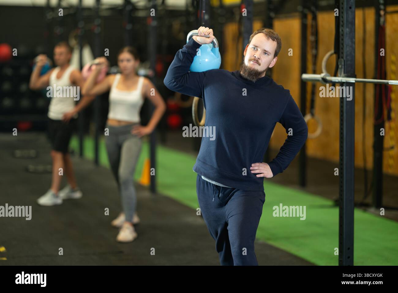 Bearded man doing kettlebell overhead shoulder press in gym Stock Photo