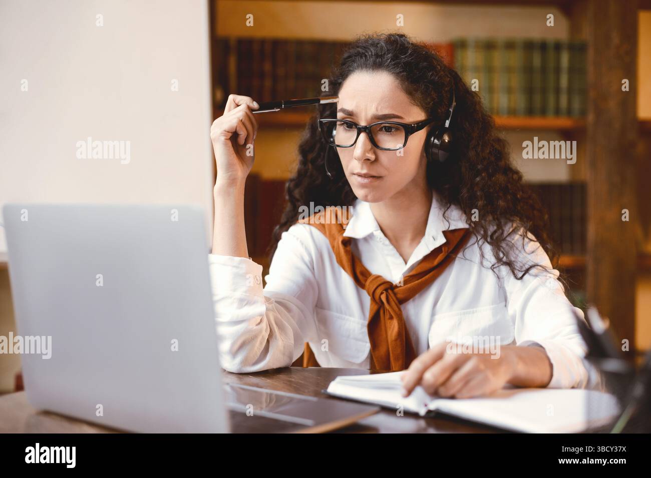 Focused woman sitting at desk, wearing headset, using computer Stock Photo
