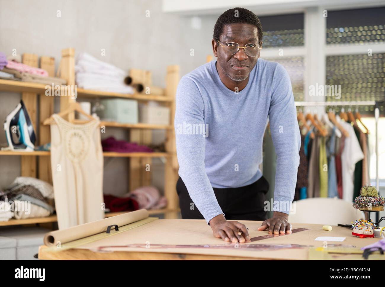 Male tailor draws sketch of future clothing on paper using patterns in sewing workshop Stock Photo