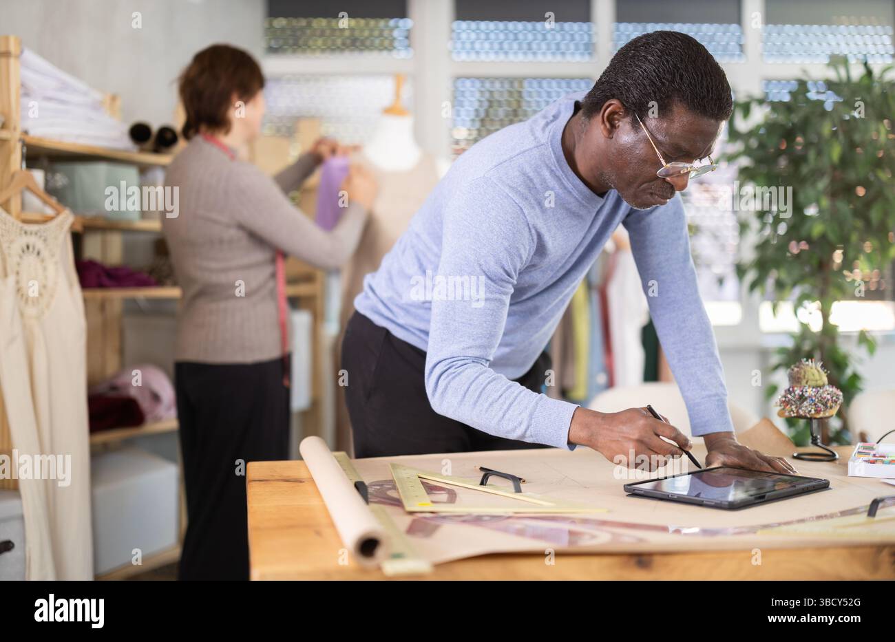 African American man tailor creates sketch of dress on tablet, woman ...