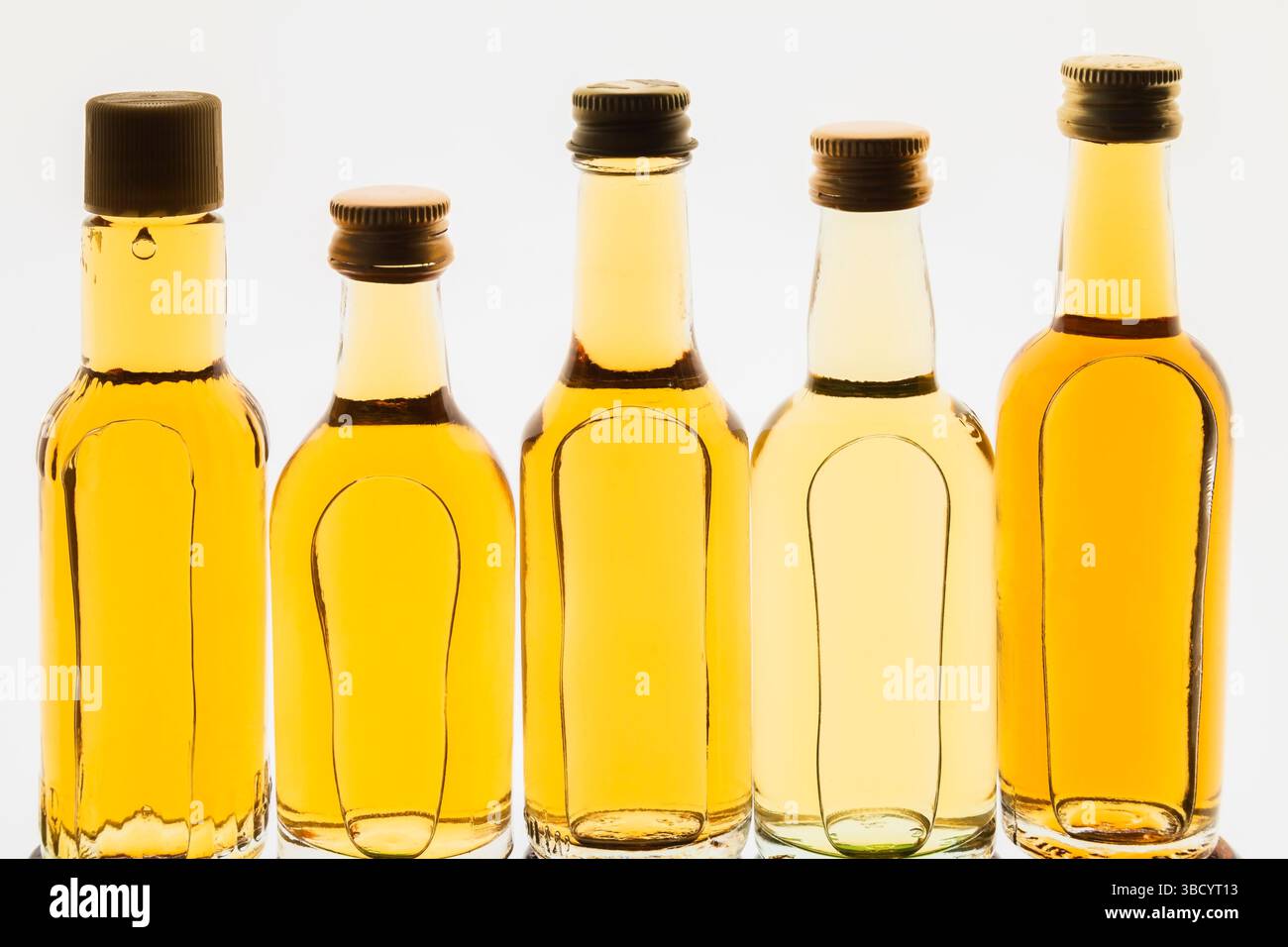 Upright miniature size golden liquor bottles on white translucent background. Stock Photo