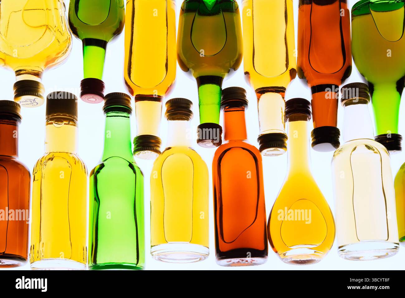 Two rows of colourful assorted shaped miniature size liquor bottles laid flat on white translucent background. Stock Photo