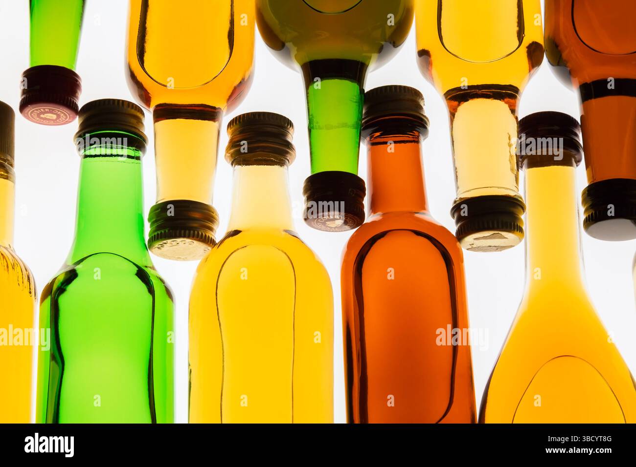 Two rows of colourful assorted shaped miniature size liquor bottles laid flat on white translucent background. Stock Photo