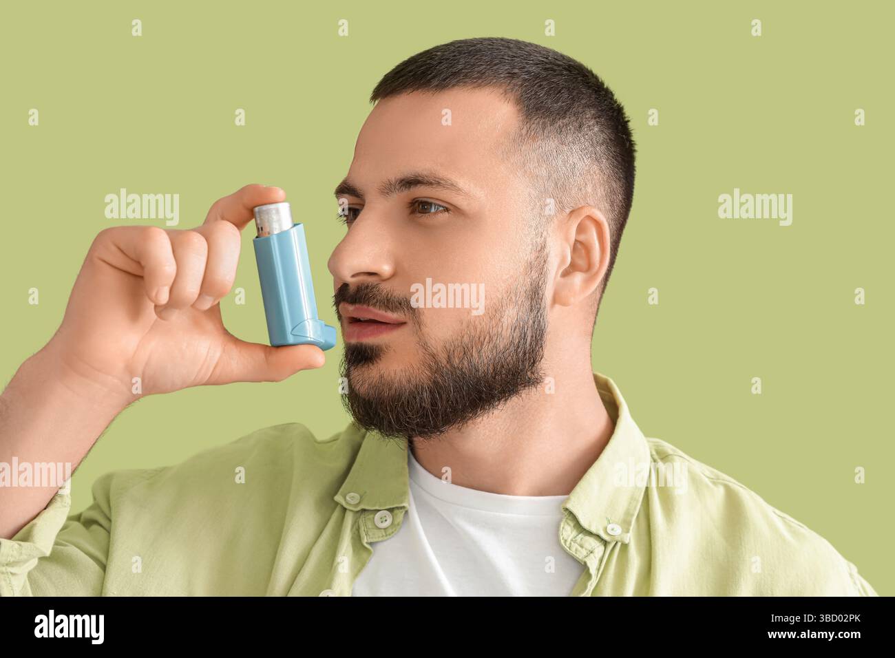Young man using inhaler on green background Stock Photo - Alamy