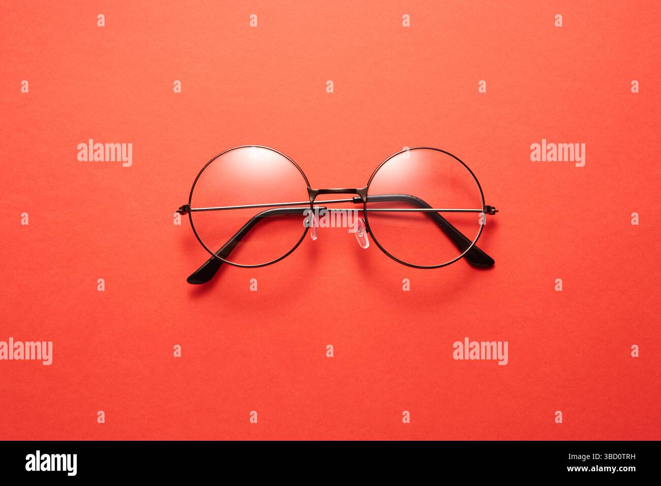 Glasses in round thin metal frame isolated on red surface. Stock Photo