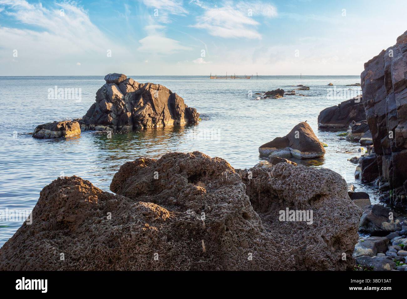seascape with rock in the water. textured boulder reflecting calm sea surface in morning light. vacation season in summer. sunny weather. fluffy cloud Stock Photo