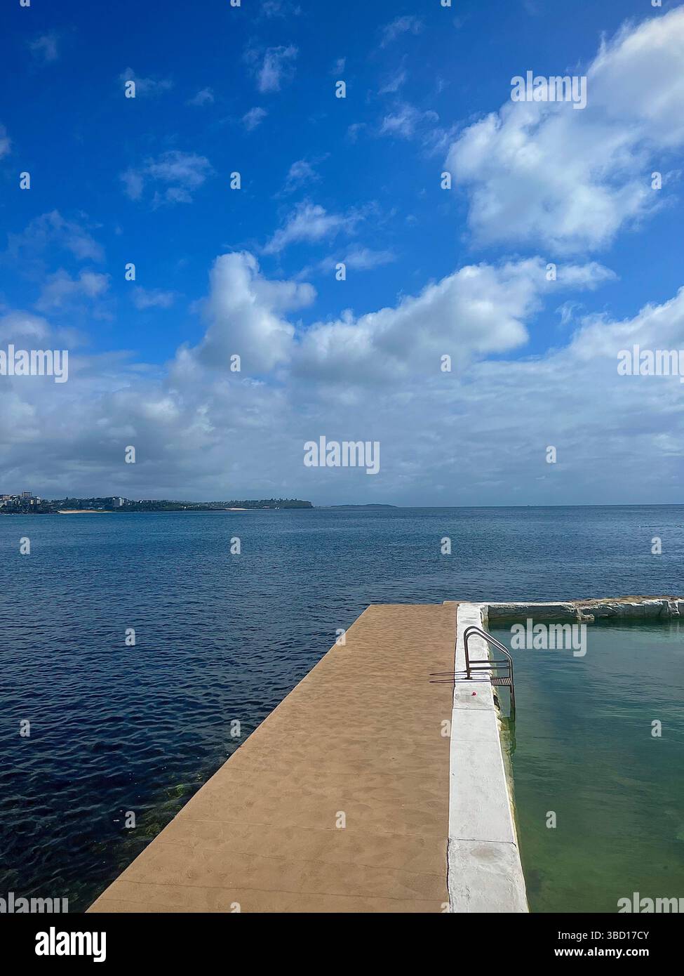 Tranquil coastal swimming pool overlooking the calm ocean under a bright blue sky with scattered clouds – a serene waterfront setting - Smartphone Captured Stock Image