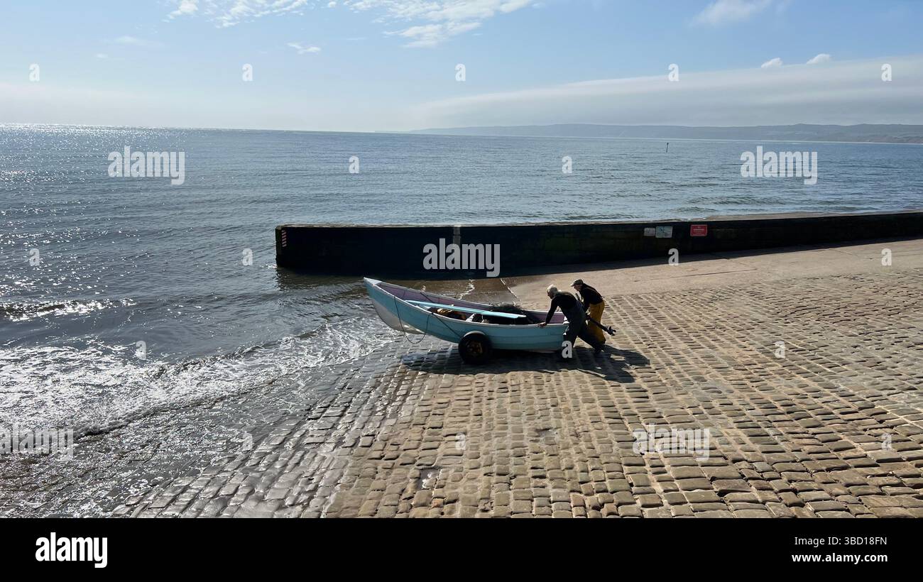 A couple of older fisher men launching a traditional clinker fishing boat at Filey, East coast of Yorkshire, northern england, UK - Smartphone Captured Stock Image