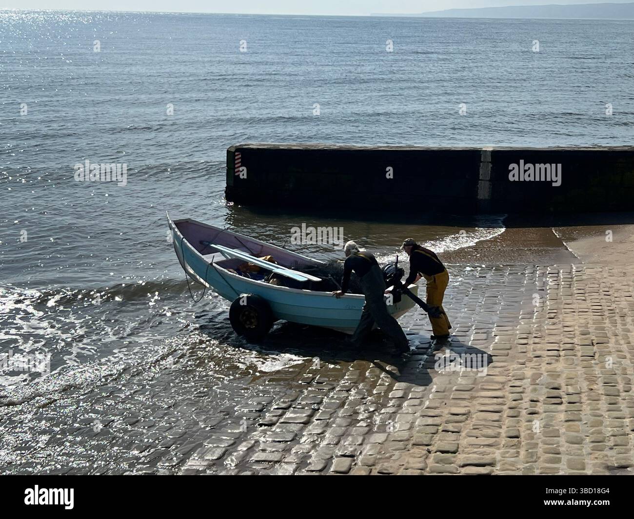 A couple of older fisher men launching a traditional clinker fishing boat at Filey, East coast of Yorkshire, northern england, UK - Smartphone Captured Stock Image
