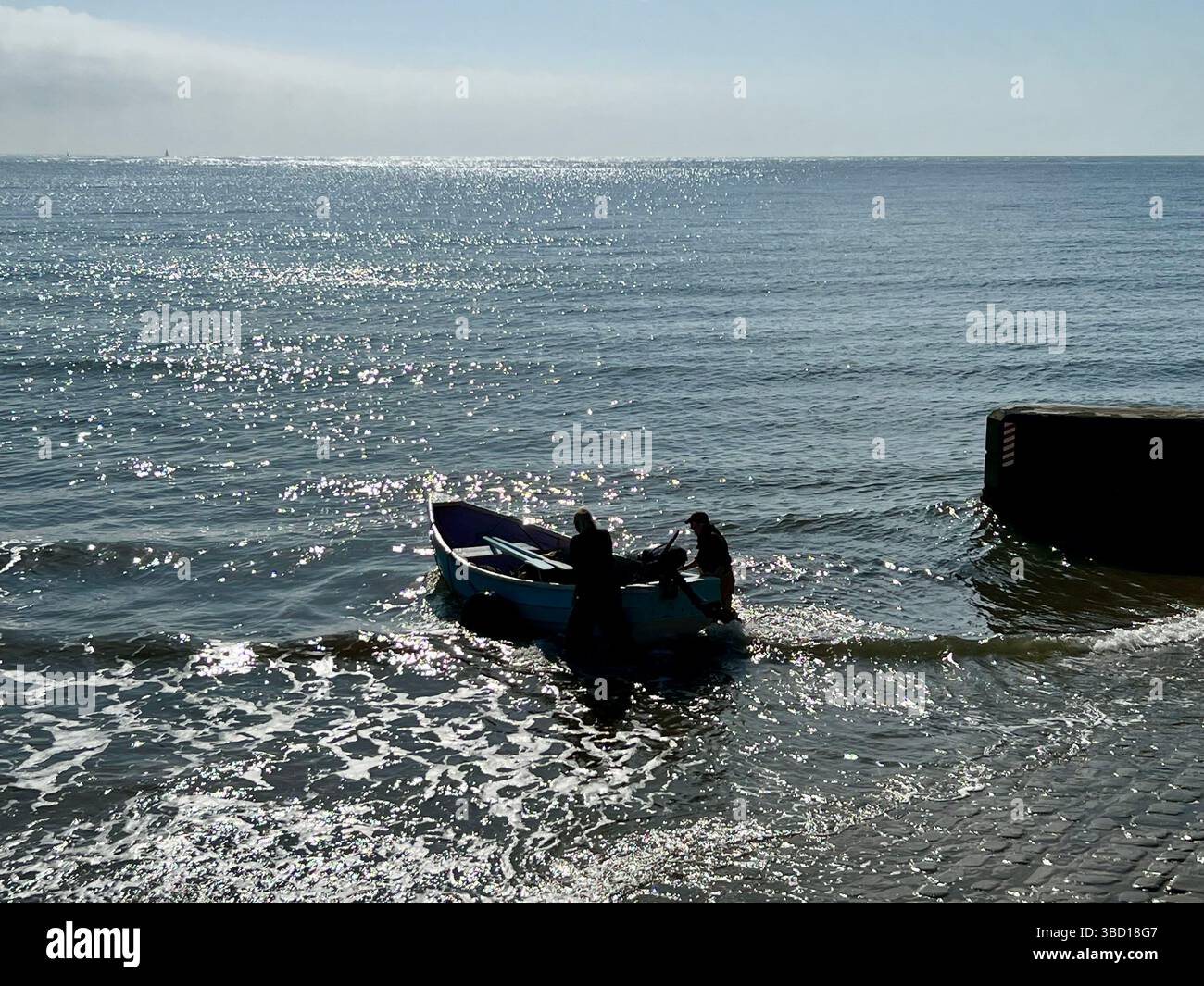 A couple of older fisher men launching a traditional clinker fishing boat at Filey, East coast of Yorkshire, northern england, UK - Smartphone Captured Stock Image