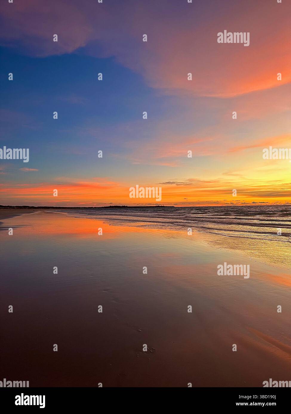 Stunning sunset over a calm beach with vibrant colors reflected on wet sand—an ideal scene for travel, wellness, and lifestyle concepts. - Smartphone Captured Stock Image