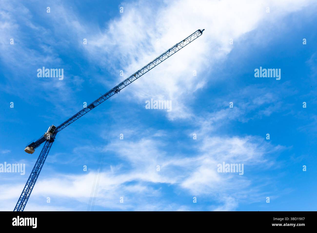Tall blue construction crane extending diagonally across a bright sky with scattered white clouds. Stock Photo