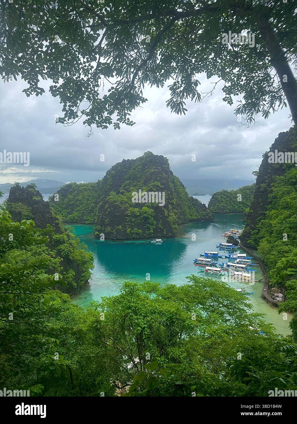 Scenic tropical lagoon surrounded by limestone cliffs and lush greenery with boats docked on turquoise water—perfect for travel and adventure themes - Smartphone Captured Stock Image