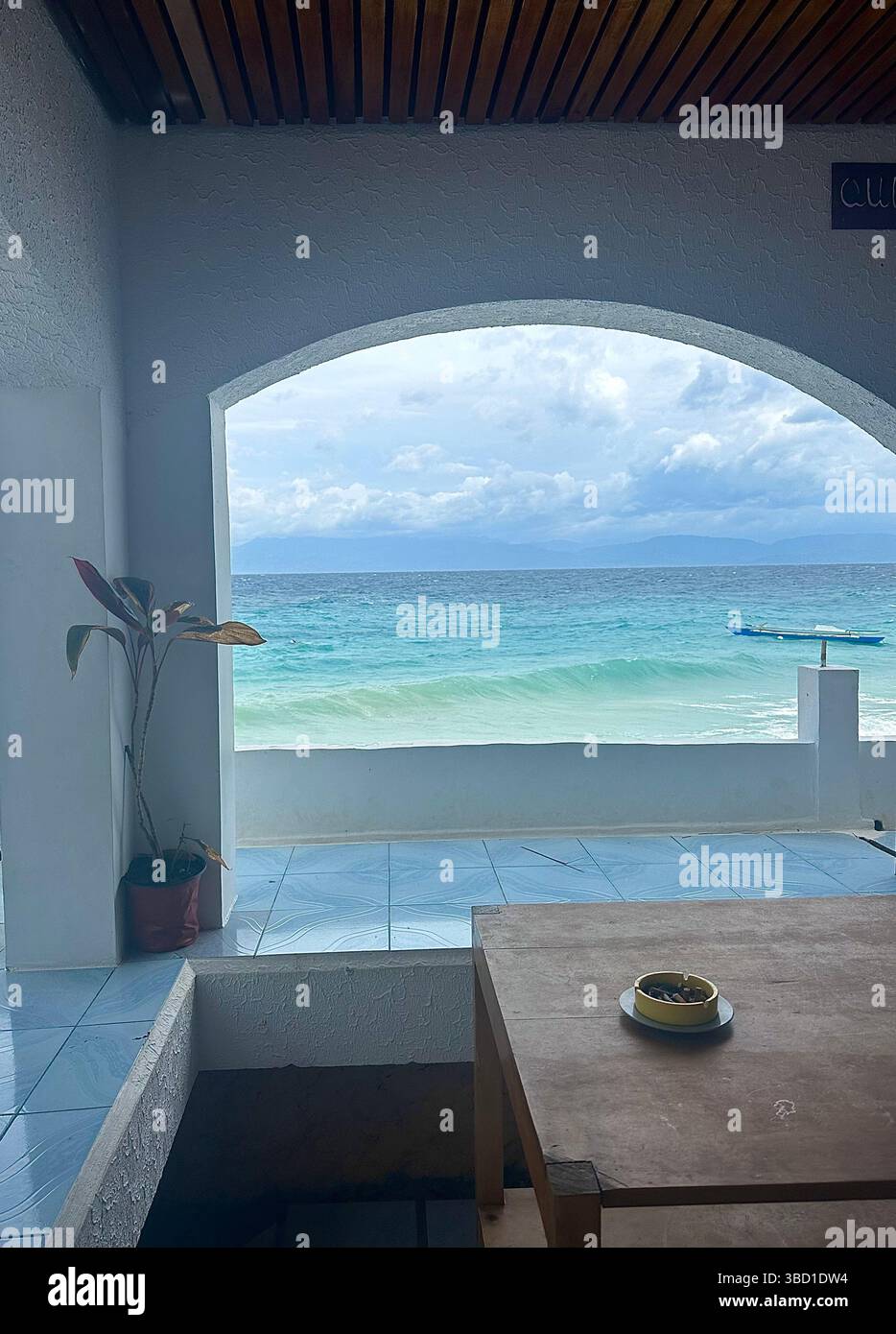 Scenic ocean view framed by a white archway from a coastal terrace, with turquoise waves and a distant boat under a cloudy sky. - Smartphone Captured Stock Image