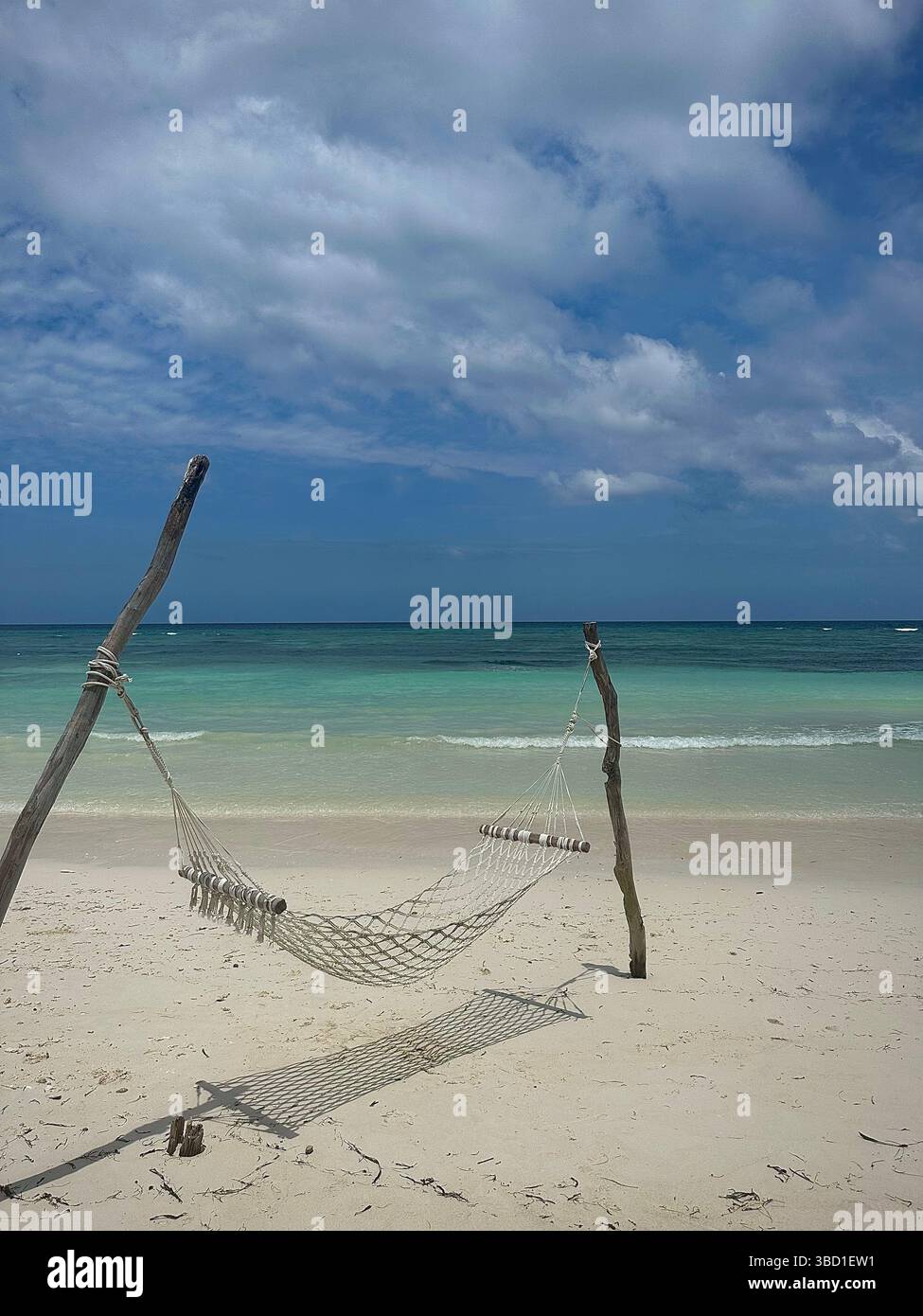 Empty hammock on a pristine tropical beach with soft white sand and turquoise ocean under a partly cloudy blue sky, evoking relaxation and escape - Smartphone Captured Stock Image