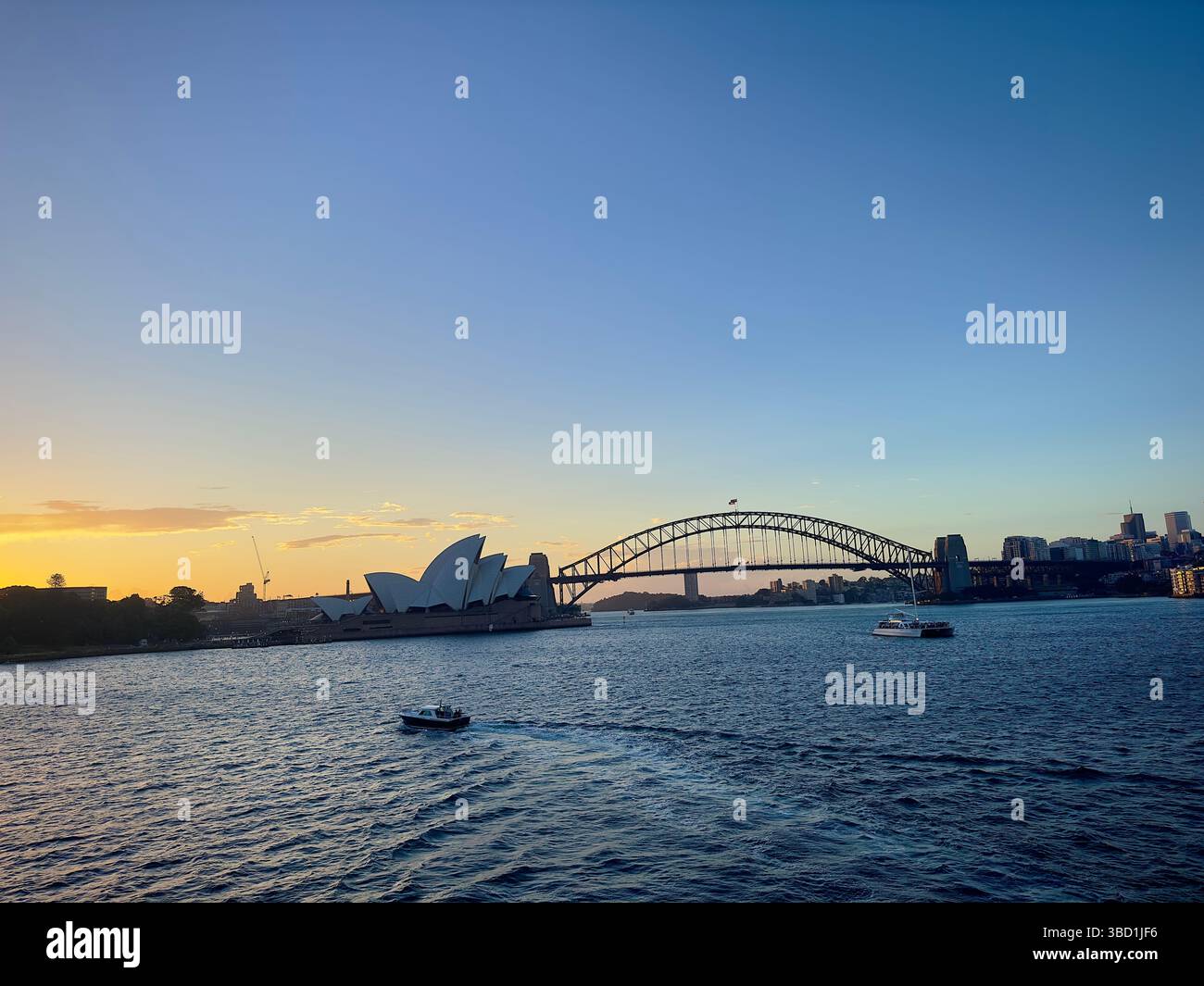Sydney Opera House and Harbour Bridge at sunset, with boats cruising across the shimmering water under a clear evening sky. - Smartphone Captured Stock Image