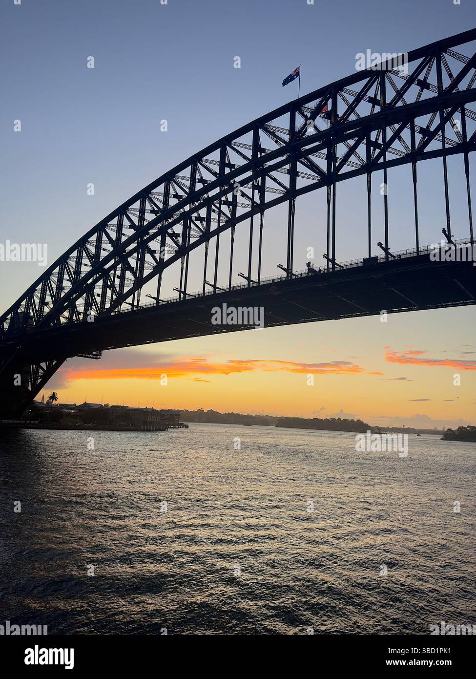 Sydney Harbour Bridge silhouetted against a colorful sunset sky, with calm harbor waters reflecting the evening light. - Smartphone Captured Stock Image